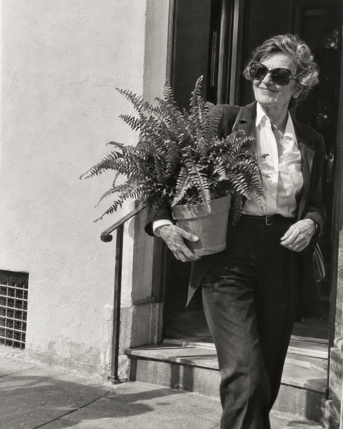 Retrato conceptual de una mujer ficticia mayor con gafas oscuras, llevando un helecho al salir a la calle