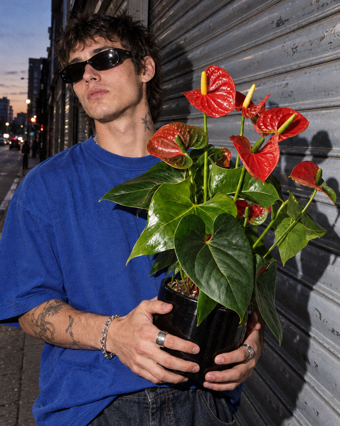 Retrato con flash de un adulto ficticio con mullet, gafas oscuras y camiseta azul, sosteniendo un anthurium rojo en maceta negra ante una persiana metálica